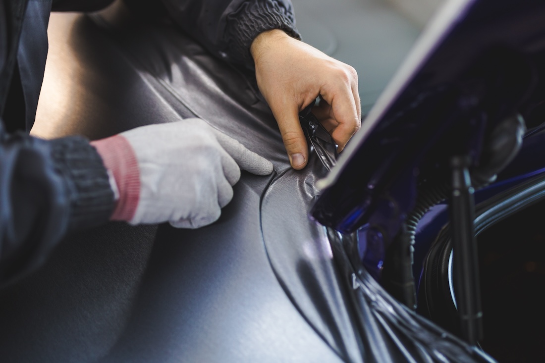 Car wrapping specialist putting vinyl foil or film on car. Selective focus.